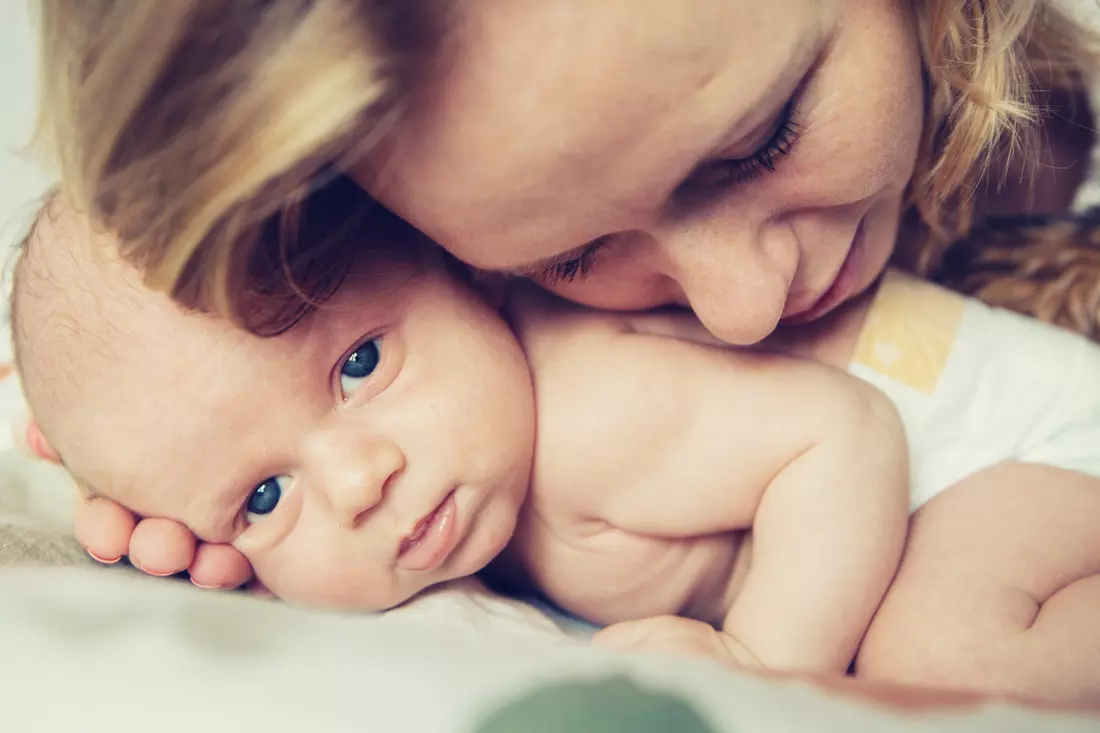 Photograph of a young mother with her newborn baby smiling happily at the camera after a successful birth with an experienced birth attendant in Miami