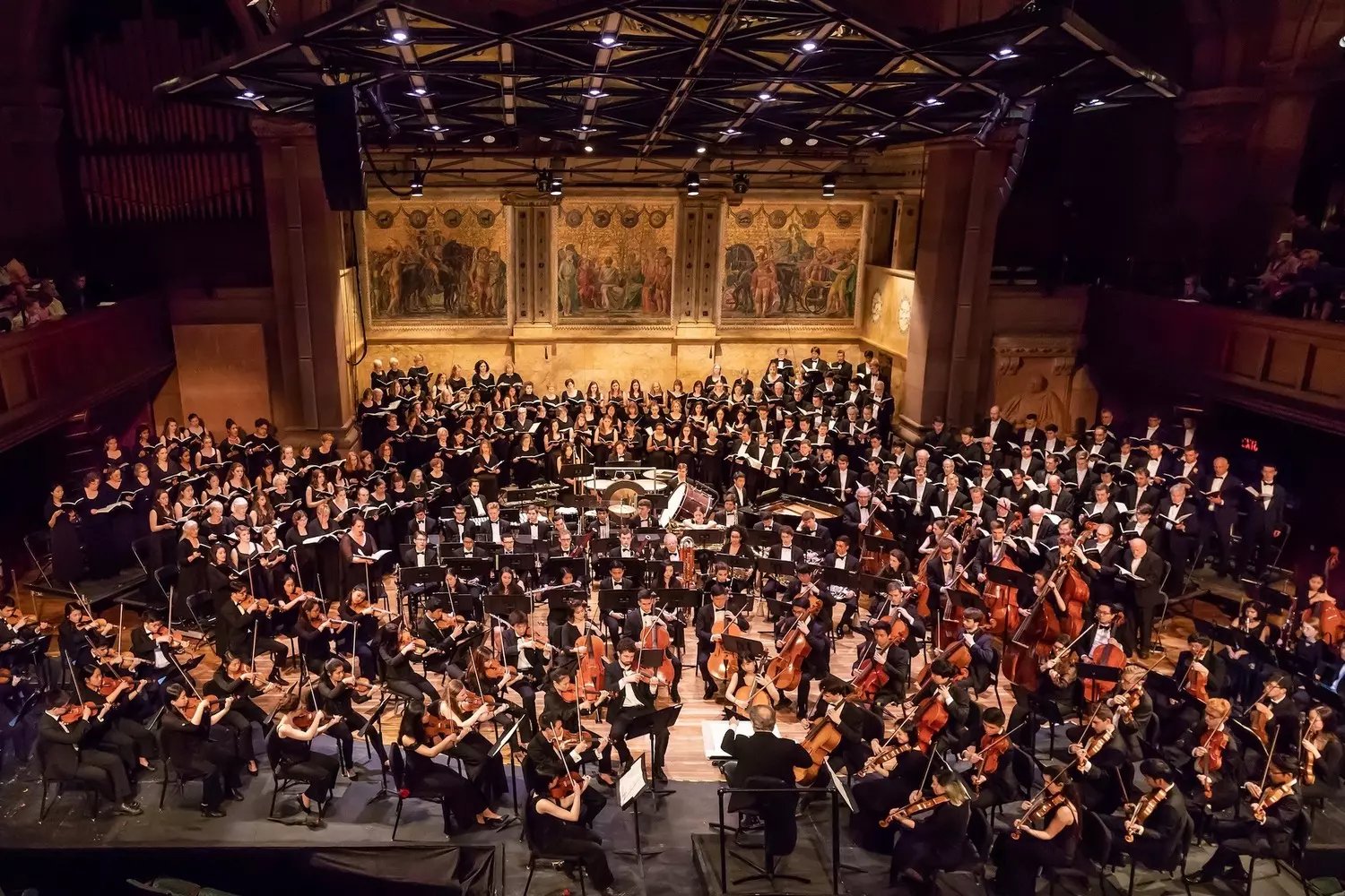 Оркестр Принстонского университета во время выступления в красивом концертном зале, дирижер руководит струнными и духовыми секциями