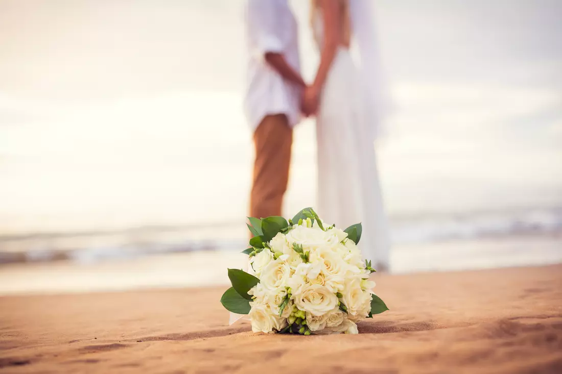 The picture shows a wedding on the beach in Miami, in the foreground you can see the bride's bouquet, in the background - the newlyweds in dresses