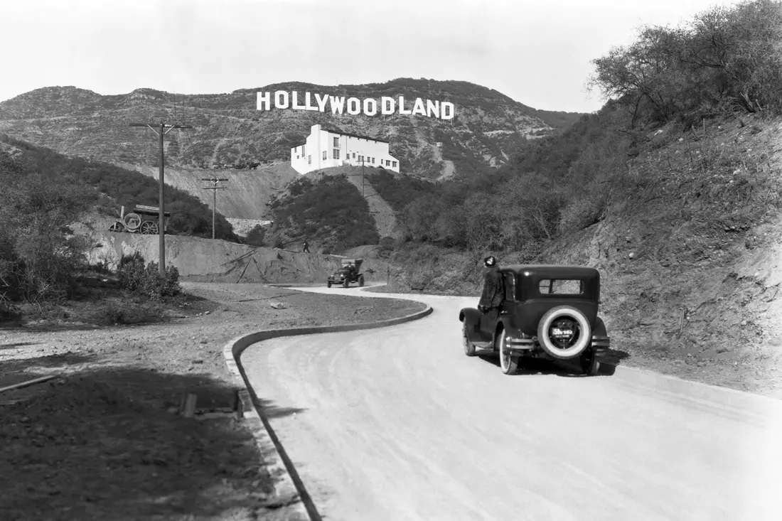 Черно-белое фото первоначального знака Hollywoodland с автомобилем 1920-х годов на переднем плане