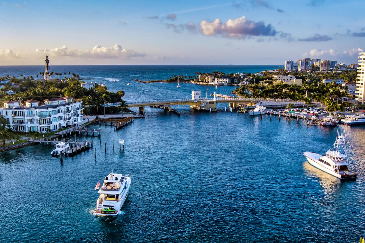 Helicopter aerial view of Fort Lauderdale's coastline featuring the Atlantic Ocean, luxury yachts docked along the waterways, a drawbridge over the canal, and tiled rooftops of waterfront homes