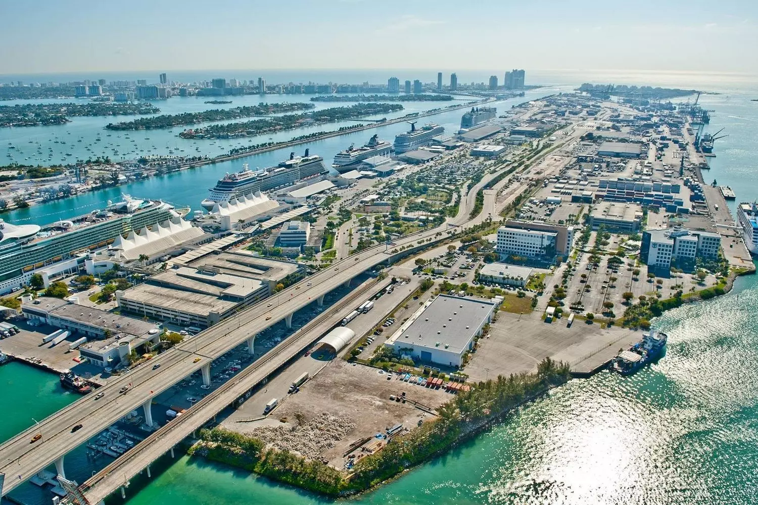PortMiami — The Cruise Capital of the World & Vibrant Waterfront Gateway Aerial view of PortMiami with massive cruise ships docked, sparkling blue waters, and the Miami skyline in the background, showcasing the bustling maritime hub