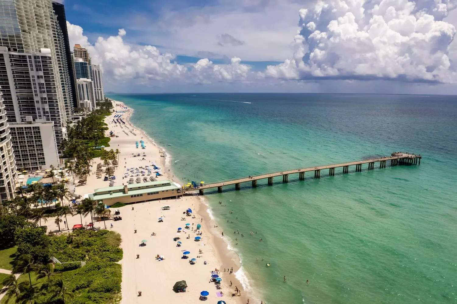 Scenic helicopter flight over Florida's shore featuring modern skyscrapers overlooking the ocean, a long causeway bridge, and turquoise waters