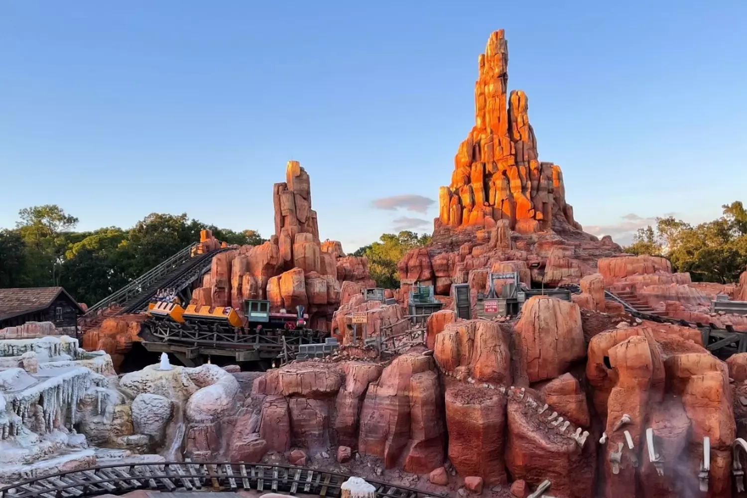 Дикий Запад в Диснейленде: Аттракцион Big Thunder Mountain Railroad в Орландо Знаменитые горки Big Thunder Mountain Railroad в стиле дикого запада с вагонетками, петляющими среди красных скал в Frontierland (Magic Kingdom, Орландо), восторженные посетители катаются на захватывающих аттракционах в солнечный день