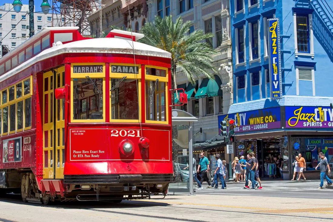 A red streetcar on Canal Street in New Orleans next to shops and palm trees