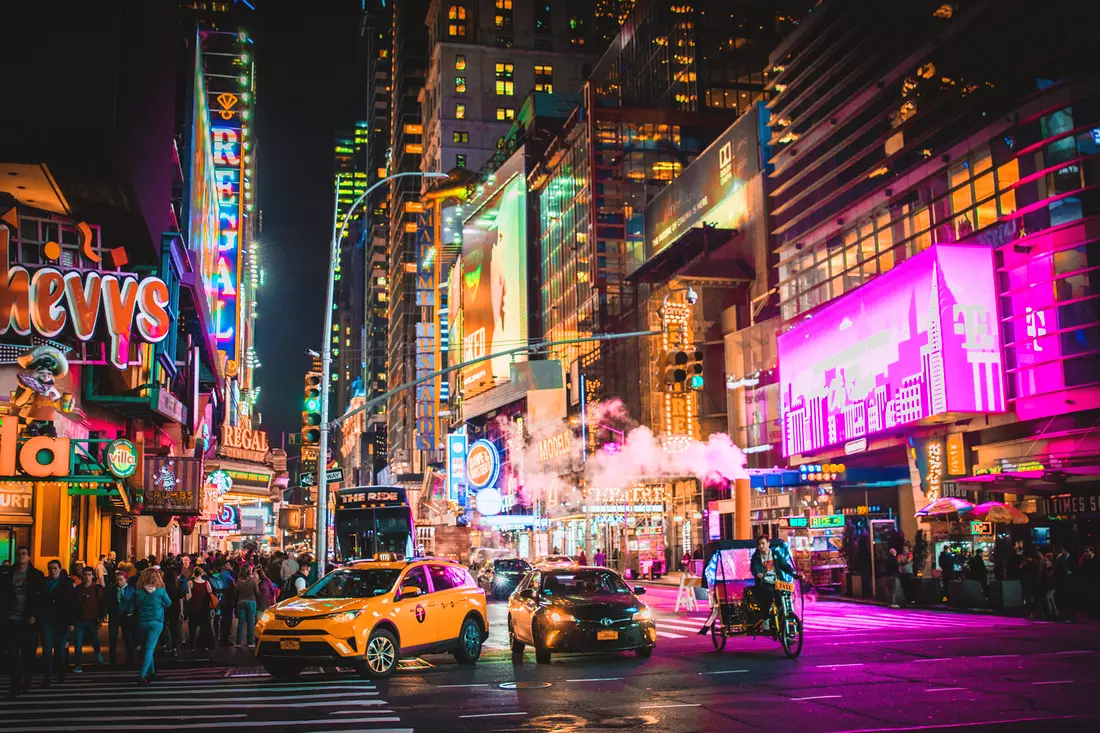 The vibrant nightlife of Broadway in New York, illuminated by neon lights and bustling with activity