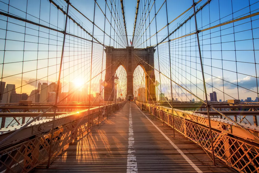 Pedestrian walkway on the Brooklyn Bridge during sunset with the city glowing