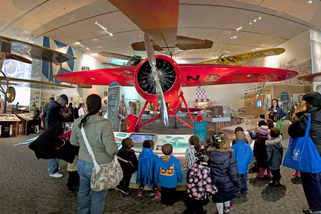 Group of children and visitors viewing a red airplane at the National Air and Space Museum