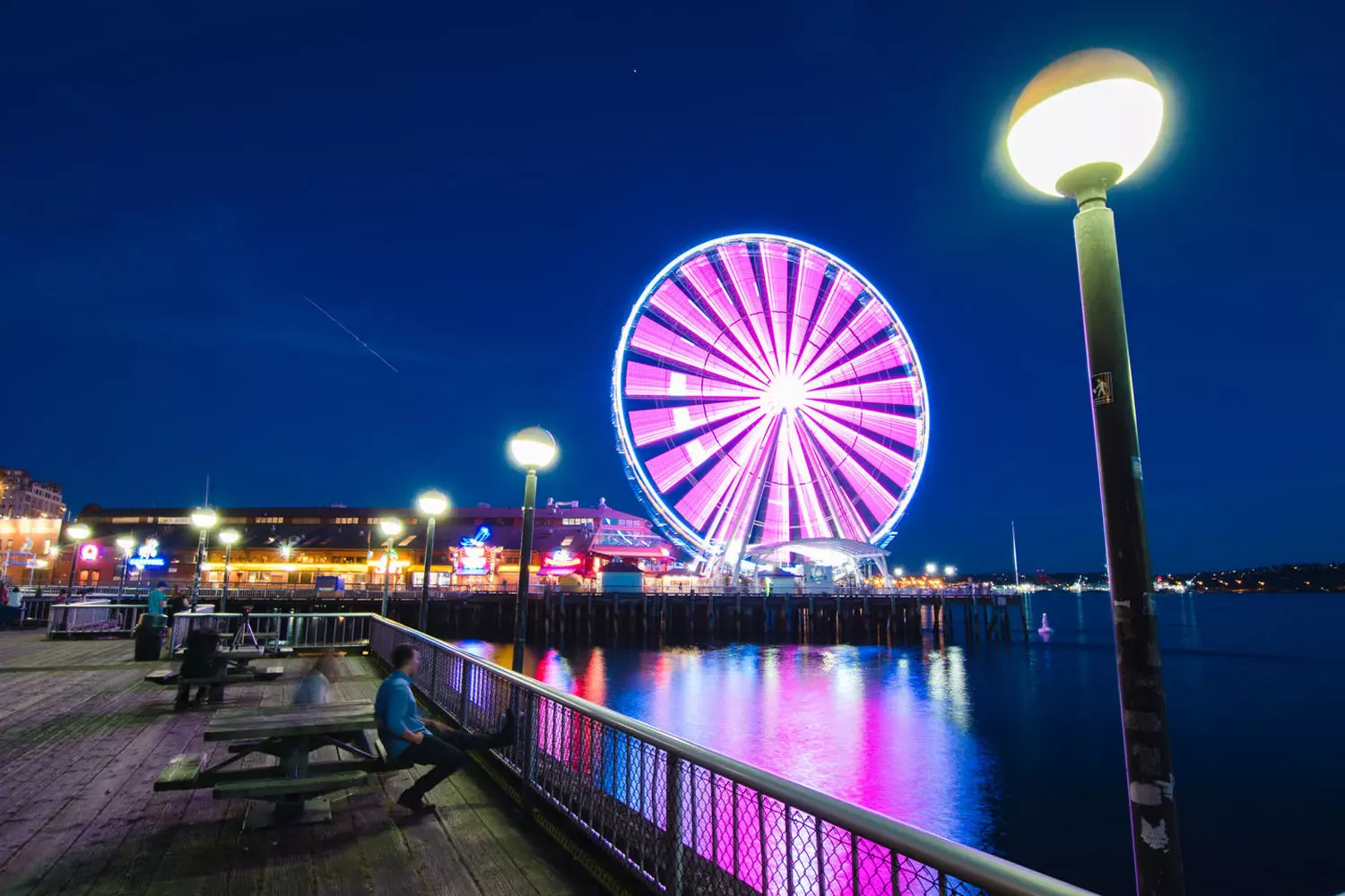 Колесо обозрения Сиэтла — Великолепные виды на набережной Колесо обозрения Seattle Great Wheel на пирсе 57, подсвеченное разноцветными огнями (или на фоне голубого неба), с видом на залив Эллиотт и силуэт города