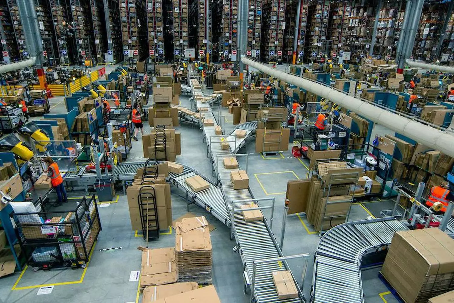 Внутри склада Amazon: как работает логистический гигант Просторный склад Amazon с рядами стеллажей, роботами и сотрудниками, собирающими заказы