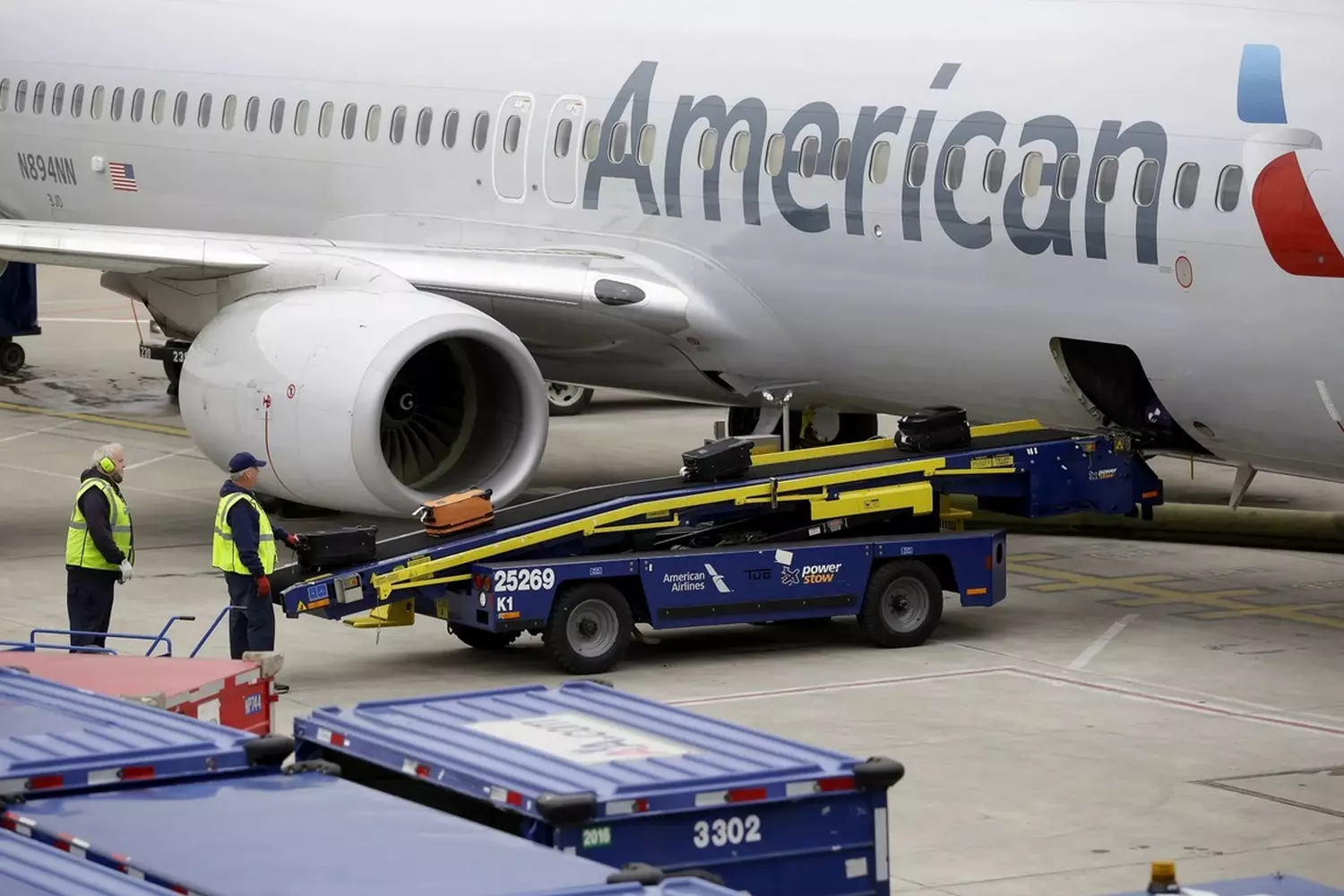 Efficient baggage handling by American Airlines ground staff American Airlines ground service team carefully loading suitcases onto a conveyor belt for aircraft loading