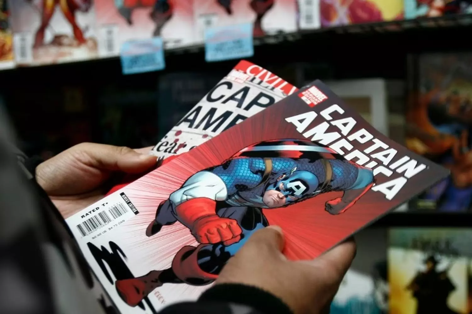 Marvel Fan Showcasing Captain America Comic Books Close-up of a man's hands holding multiple Captain America comic books from Marvel Comics, highlighting the evolution of the character's design over the years