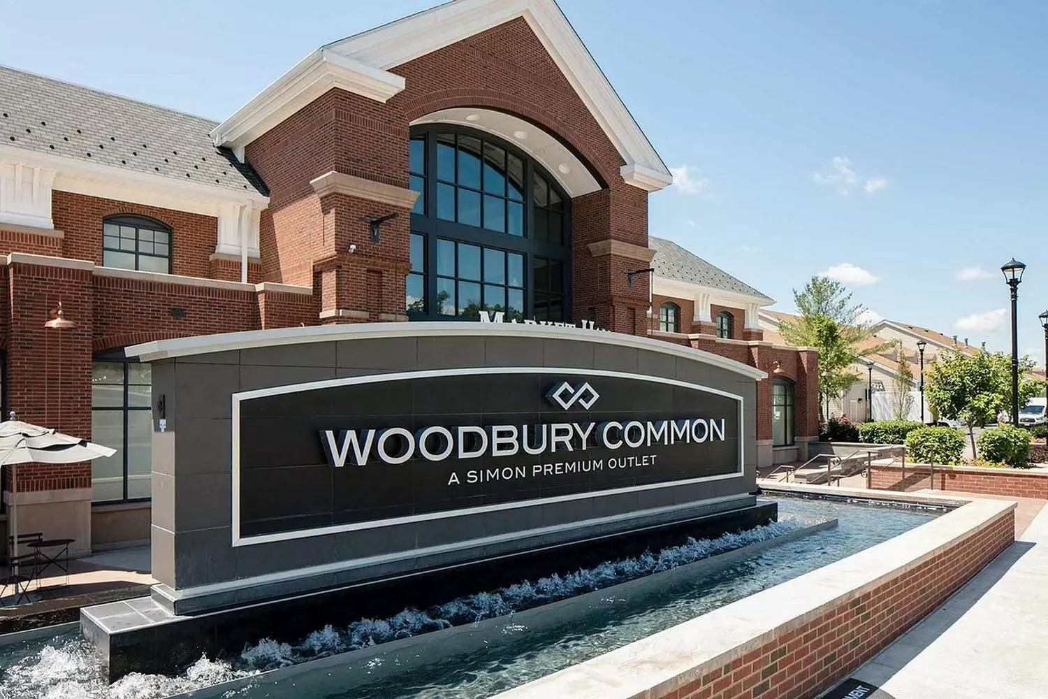 Woodbury Common Premium Outlets: роскошный шопинг на открытом воздухе Вид с высоты на Woodbury Common Premium Outlets: аллеи бутиков мировых брендов, ухоженные пешеходные дорожки и покупатели, наслаждающиеся шопингом со скидками в формате open-air