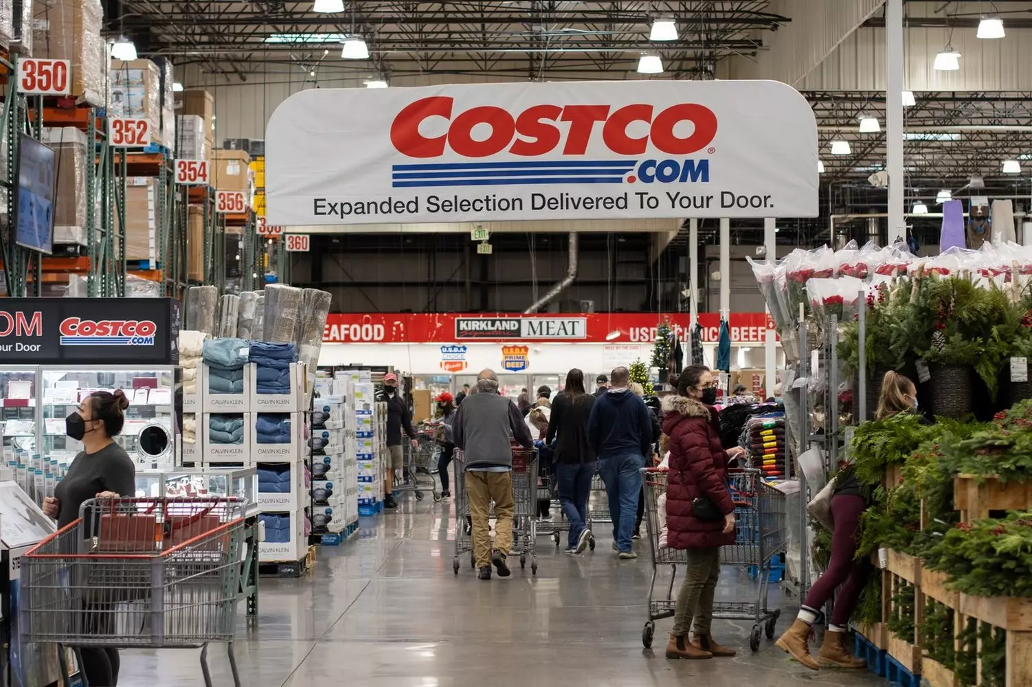Inside Costco USA: A Look at America's Iconic Warehouse Shopping Experience Spacious interior of a Costco wholesale store in the USA, showcasing high shelves stocked with bulk products, shopping carts filled with oversized items, and members browsing under bright warehouse lighting