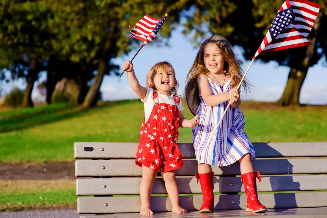 Two young girls joyfully celebrating with American flags outdoors