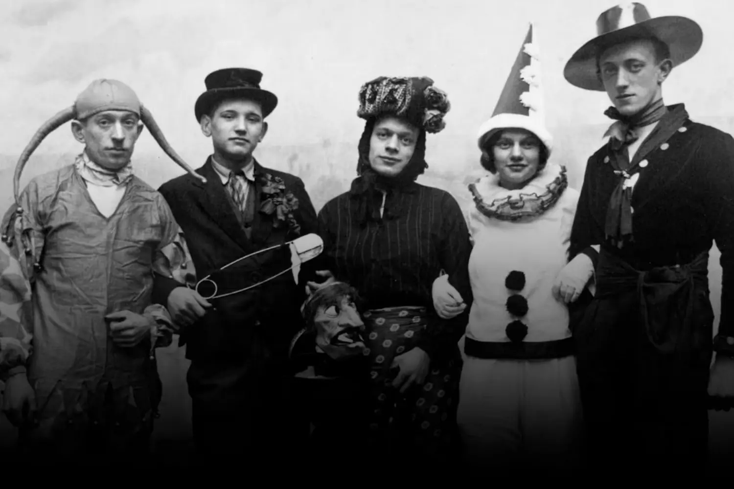 Vintage Halloween Spookiness: Bizarre Costumes from the Past Black-and-white historical photo of people in unusual early 20th-century Halloween costumes, including eerie masks and homemade outfits, celebrating the holiday in a vintage style