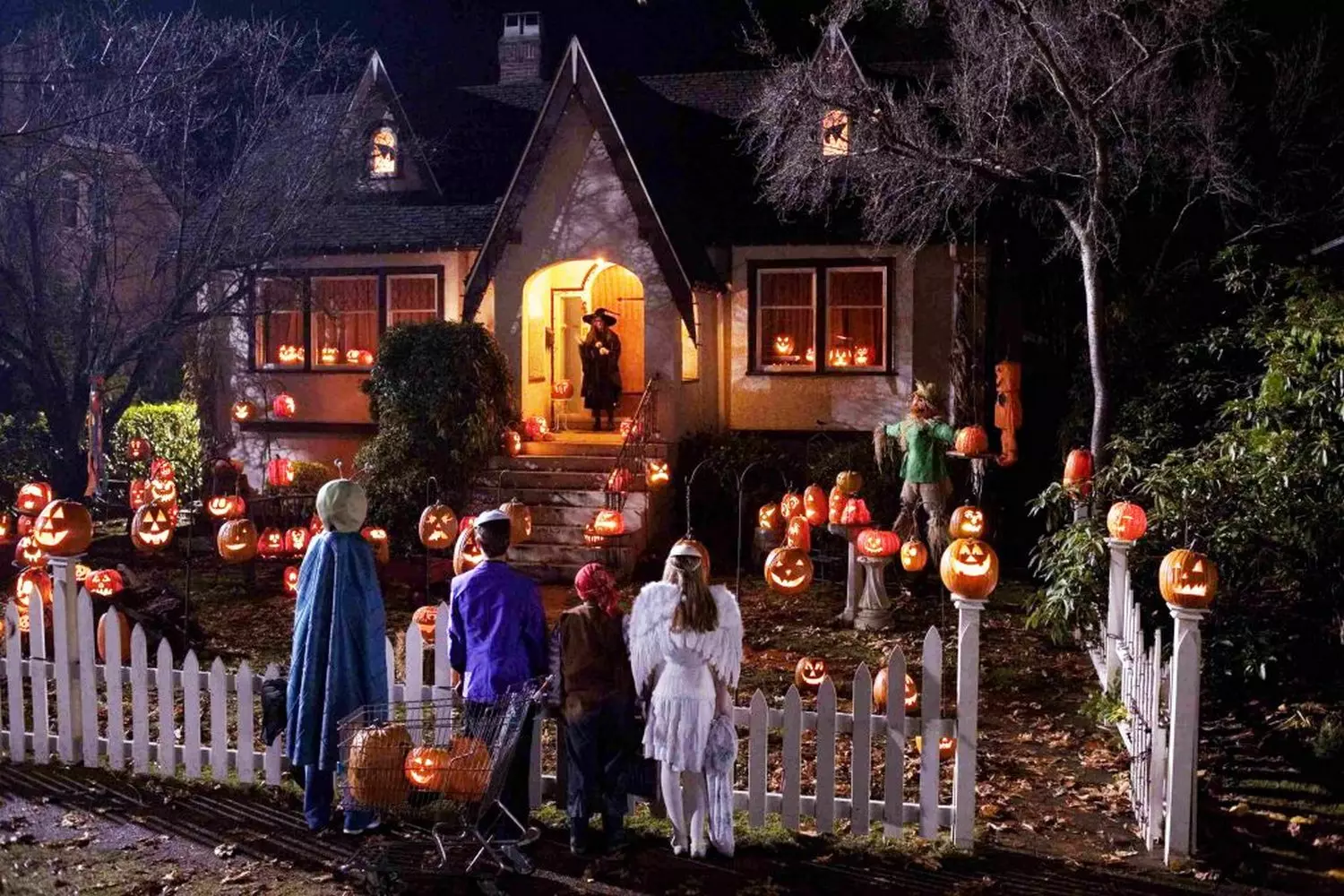 Ultimate Halloween House: Spooktacular Decorations & Lights A lavishly decorated house for Halloween with orange lights, giant spiders, cobwebs, jack-o'-lanterns, and spooky silhouettes in the windows, creating a festive haunted atmosphere