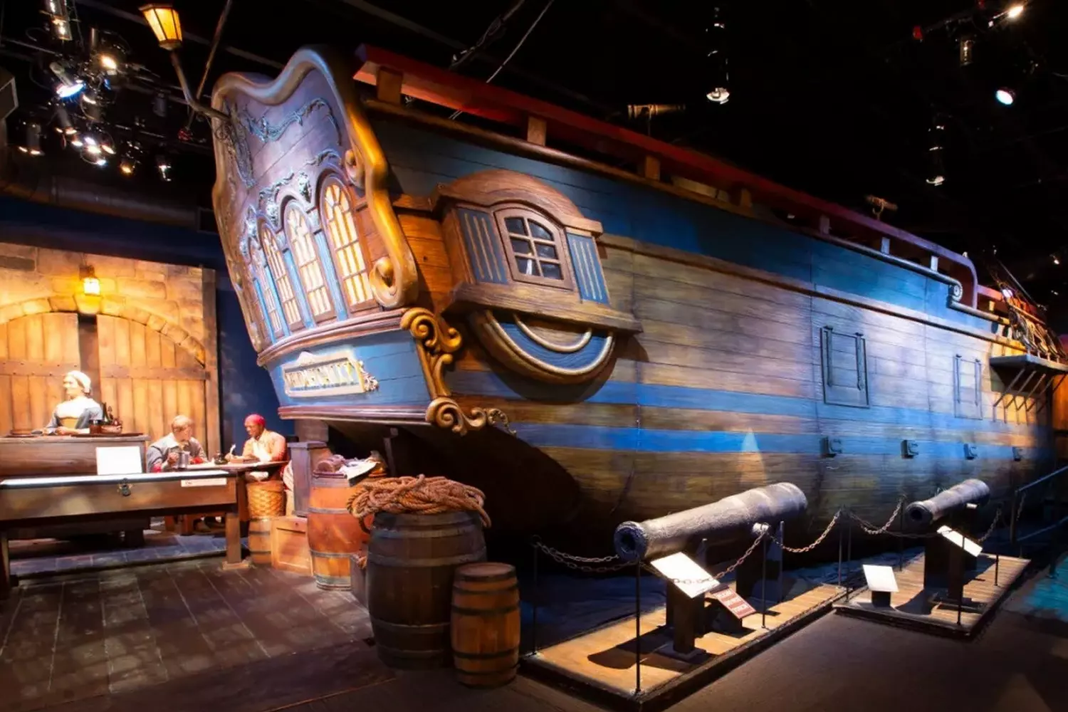 Life On Board: Interactive Exhibition of Pirate Ship and Sea Robbers' Daily Life in Museum Museum exhibition featuring full-scale pirate ship surrounded by sketches of pirate daily life: loot division, navigation, ship repair, and tavern feast