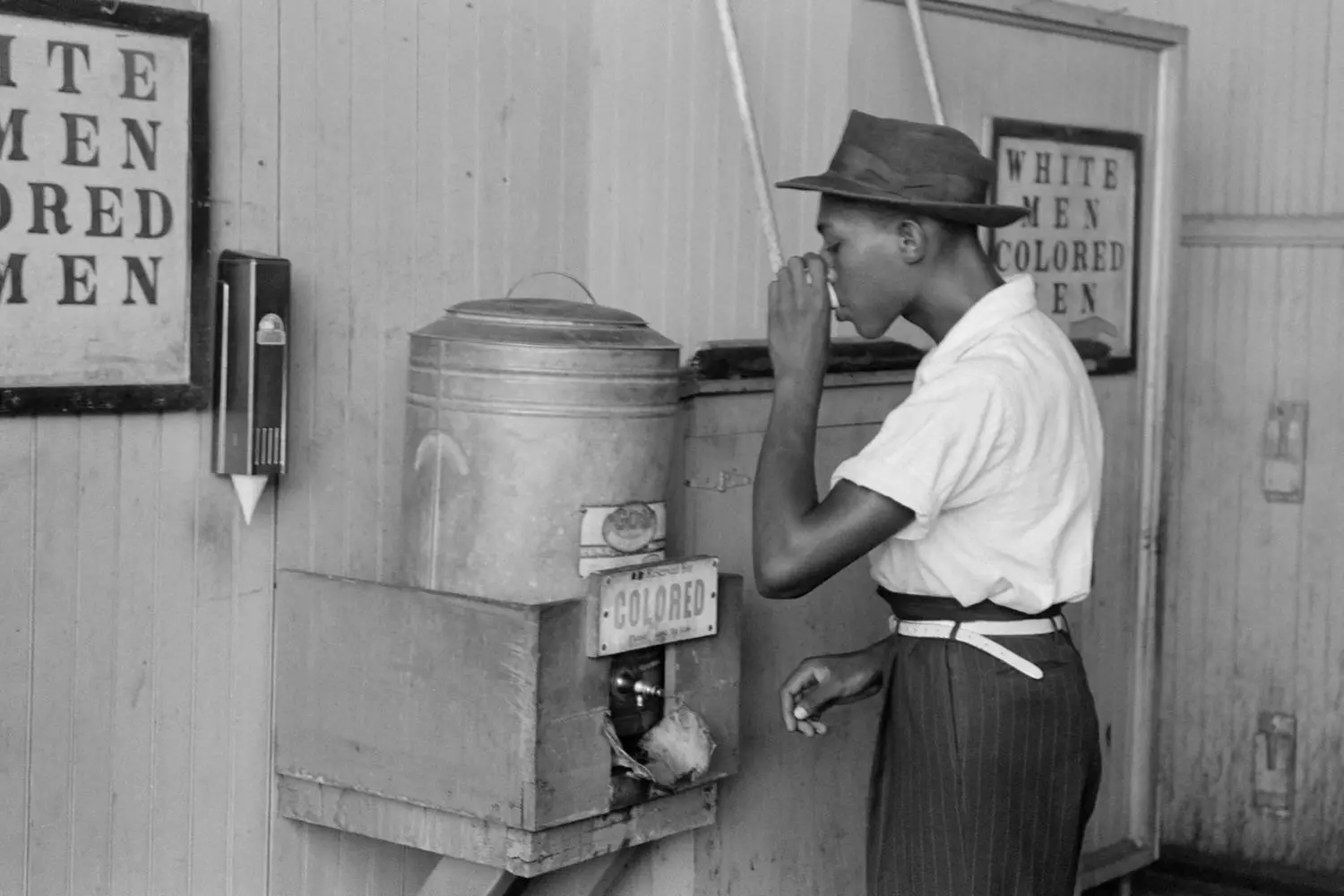 The Era of Racial Segregation in the USA — a man drinking from a 'For Colored Only' fountain Historical photograph showing racial segregation in the USA: an African American drinking from a water fountain with a sign 'For Colored Only' during the Jim Crow laws era