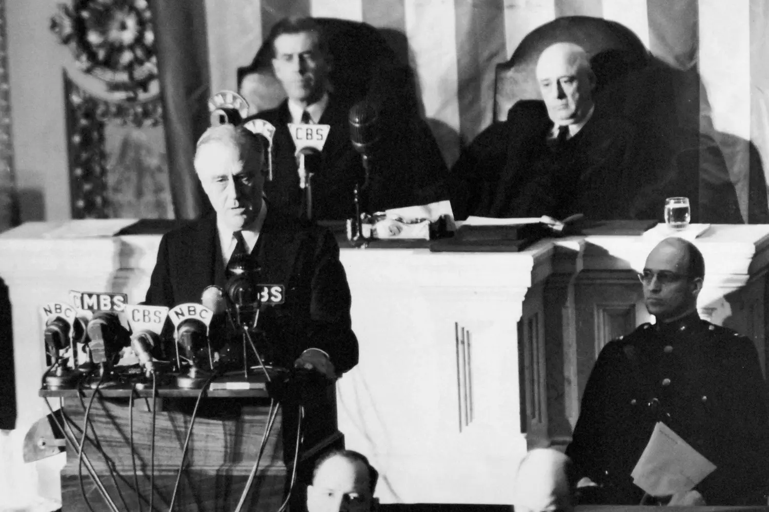 FDR Addresses the Nation: America on the Brink of War U.S. President Franklin D. Roosevelt delivering a solemn pre-war speech, possibly to Congress or a public rally. The American flag is visible in the background