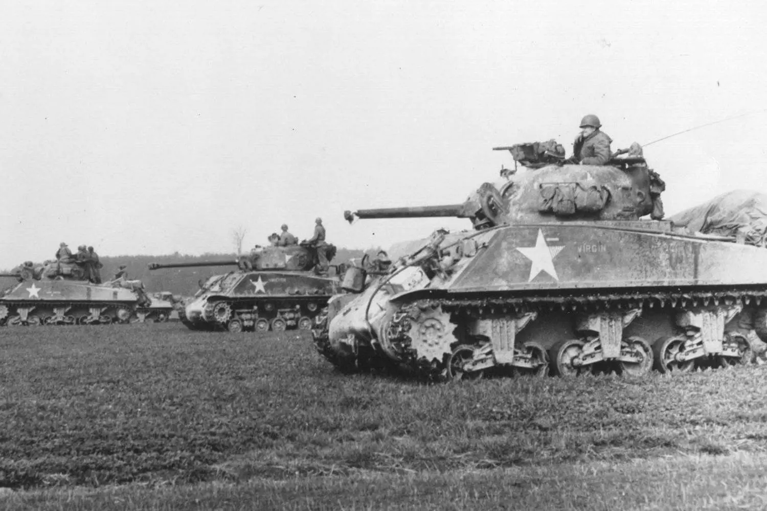 The M4 Sherman: America's Iconic WWII Battle Tank An M4 Sherman medium tank advancing through a battlefield. Distinctive angular turret with 75mm gun, tracks with V-shaped cleats