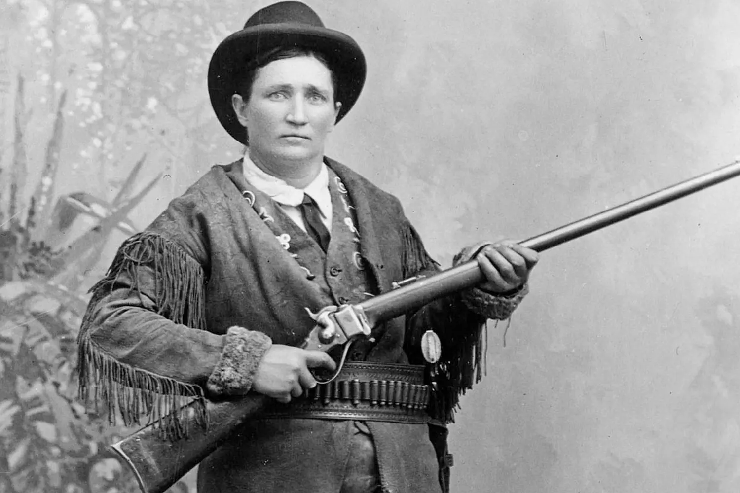 Historic Photo of Calamity Jane in Her Classic Look A black and white portrait of Martha Jane Cannary, known as Calamity Jane, dressed in her signature fringed buckskin jacket and holding a rifle, with a determined expression on her face