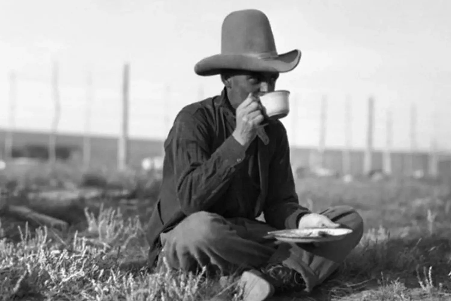 A Moment of Rest: Cowboy's Lunch Break on the Prairie A lone cowboy on a lunch break, sitting on the ground and eating by his saddled horse in a vast prairie under the sun