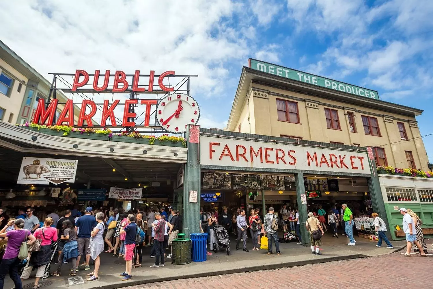 Оживленная субботняя сцена на community-рынке: люди общаются, несут холщовые сумки, полные свежих продуктов