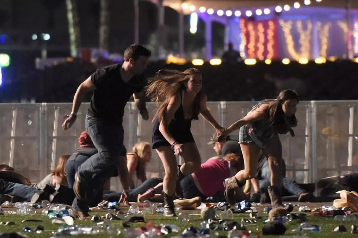 Chaos Under the Neon Lights: Concertgoers Flee During Route 91 Harvest Festival Shooting Blurred image of dozens of people running desperately across an open field at night, some falling, as bright stage lights illuminate the chaos during the Route 91 Harvest festival shooting