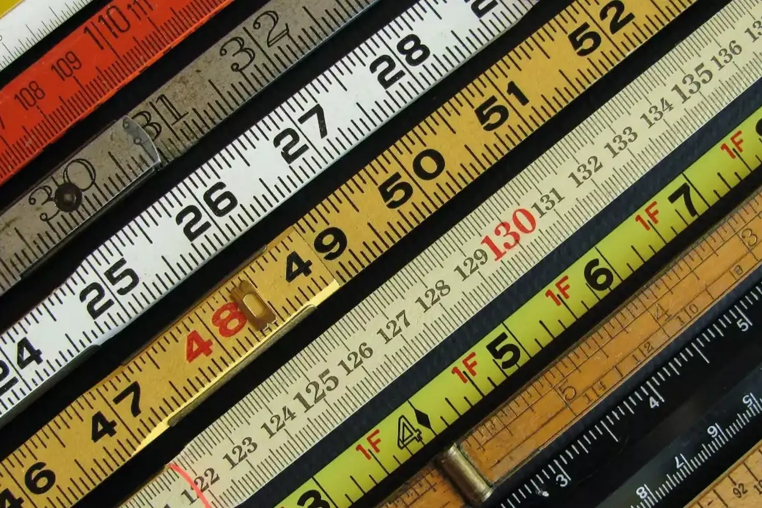 Imperial vs Metric: Side-by-Side Comparison of American and International Rulers Three wooden rulers placed side by side showing inches (imperial system), centimeters (metric system), and dual-scale measurements for comparison