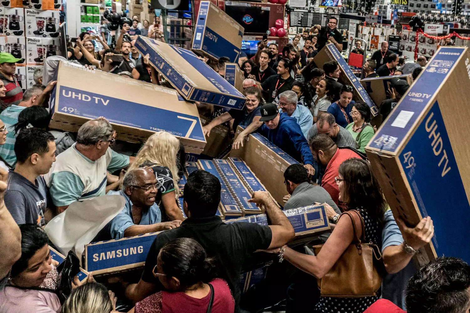 An electronics store during the first hours of Black Friday sales: customers running towards shelves with TVs and laptops