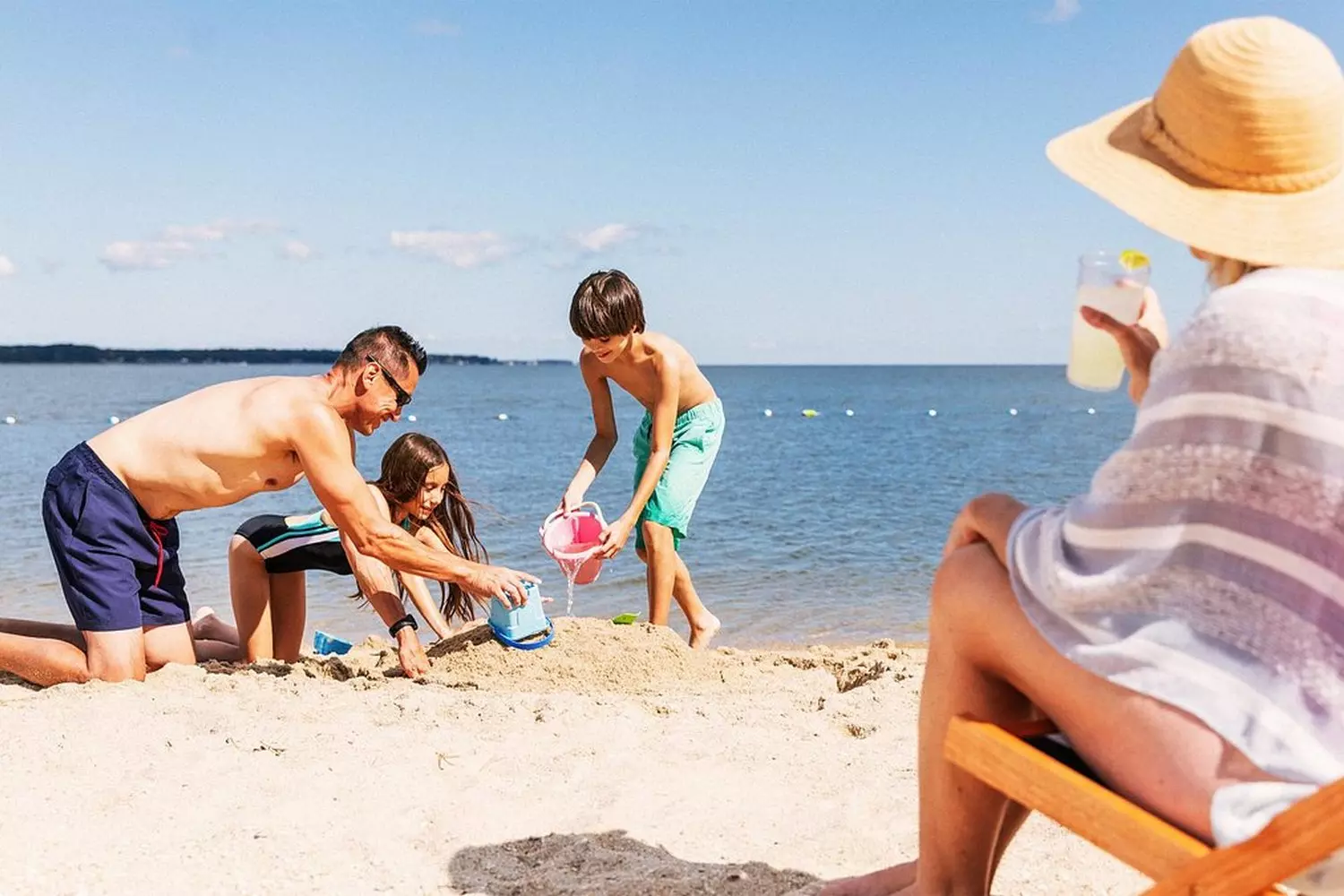 Счастливая семья с двумя детьми играет на песчаном пляже с волнами у океана в США