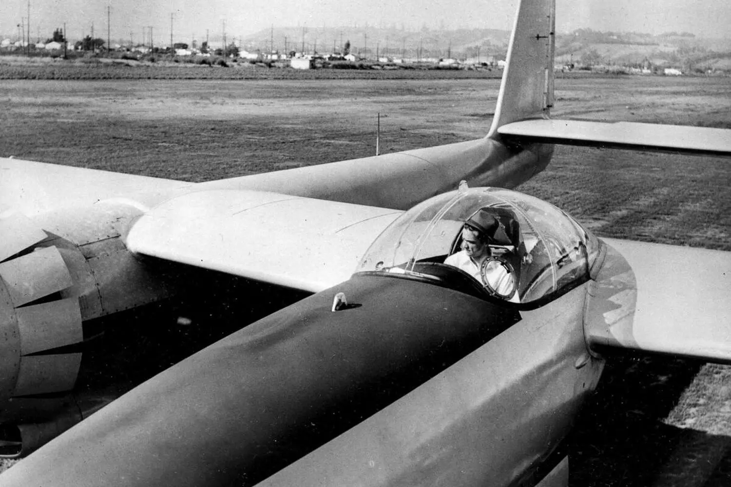 Howard Hughes in the Cockpit: The Aviator at His Natural Habitat Black-and-white photo of Howard Hughes sitting in the cockpit of his aircraft, hands on controls, with intense focus — capturing his legendary passion for aviation and engineering