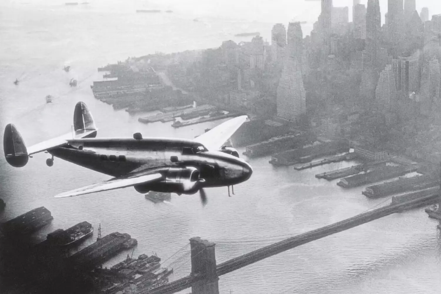 Howard Hughes' Magnificent Flying Machine Conquers the Skies Vintage black-and-white photo of Howard Hughes' iconic aircraft soaring through the clouds, symbolizing his groundbreaking contributions to aviation history