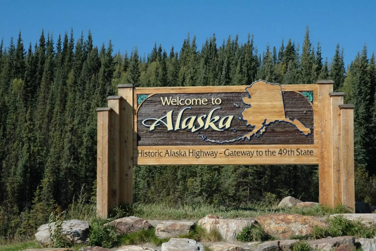 Welcome to Alaska: The Last Frontier A rustic 'Welcome to Alaska' sign with wooden letters against a backdrop of snowy mountains and evergreen trees, embodying the wild spirit of America's northernmost state