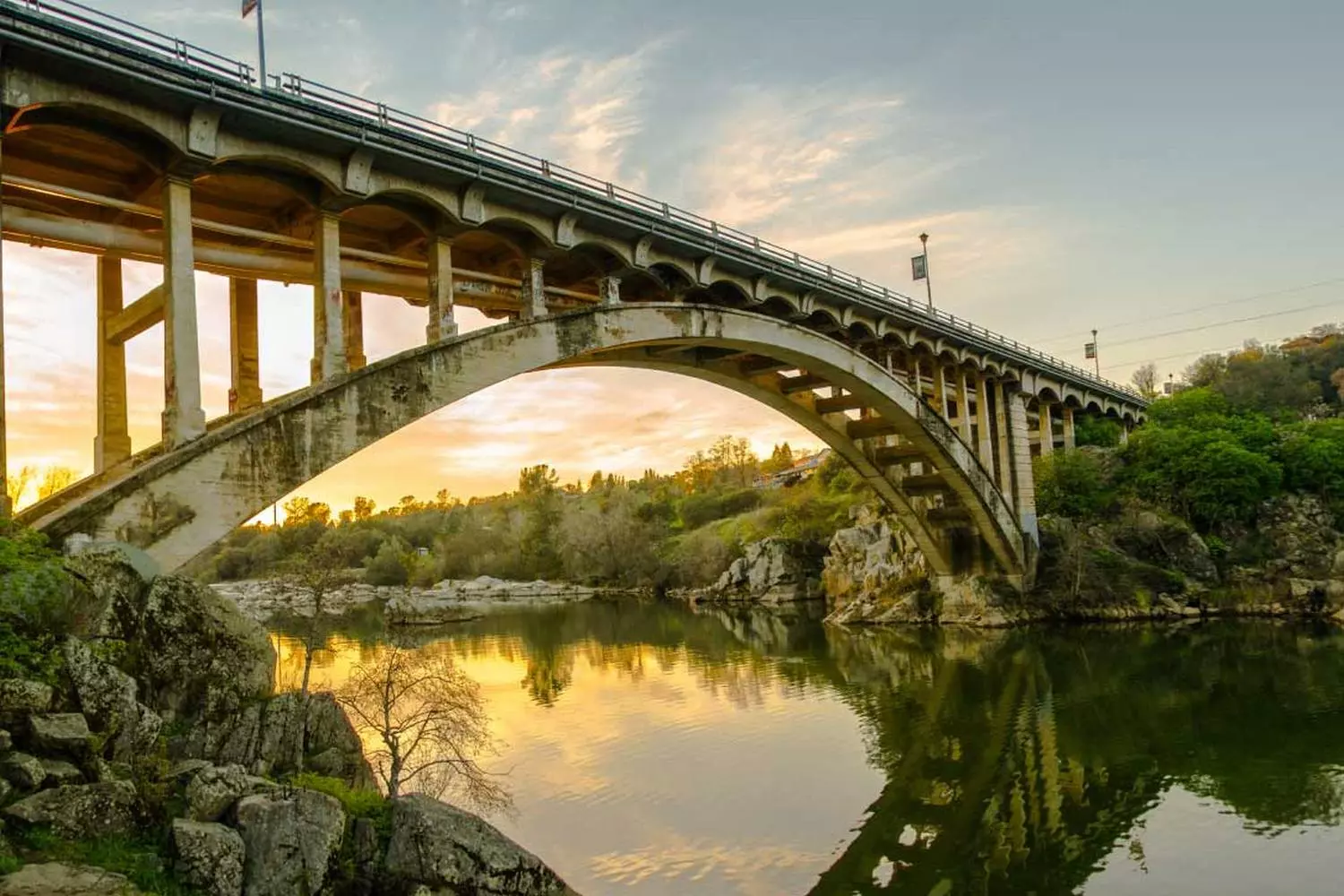 Famous Rainbow Bridge arch bridge over Lake Natoma in Folsom, California, during the day with water and hills in the background