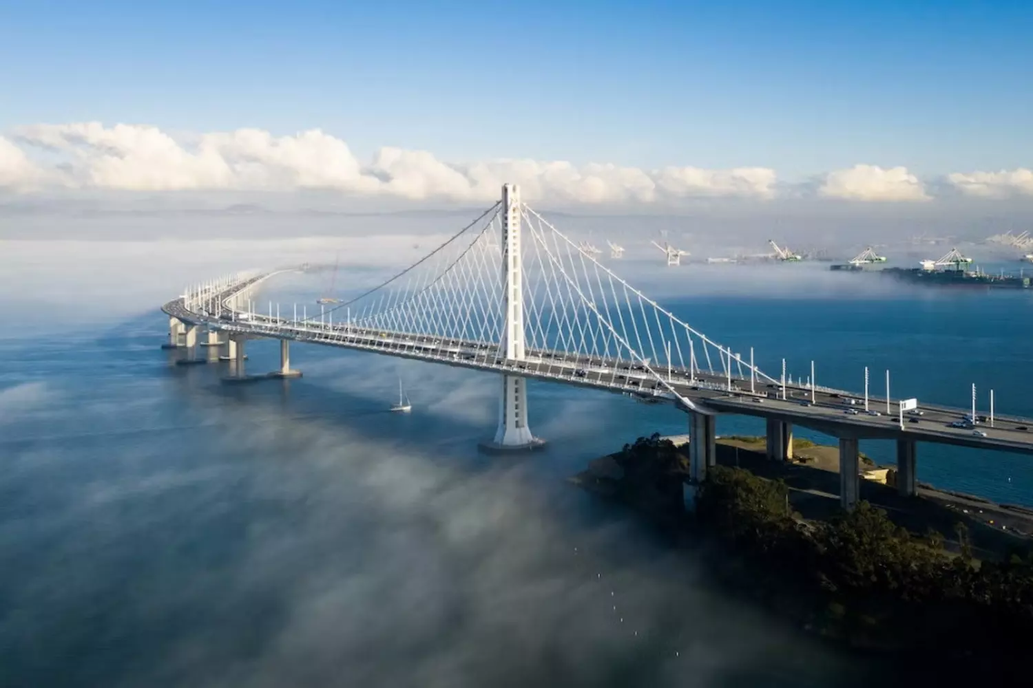 Bay Bridge during the day with San Francisco skyline in the background, steel trusses and busy traffic