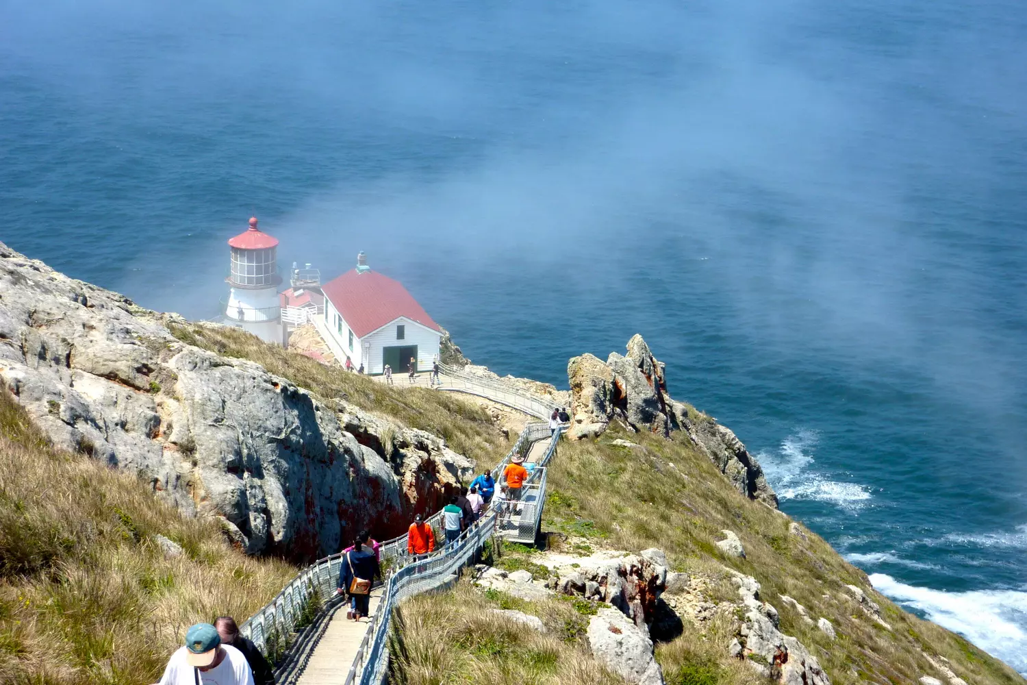 Tourists walking along the trail toward Pigeon Point Lighthouse, the tallest white tower on the California coast, ocean and cliffs