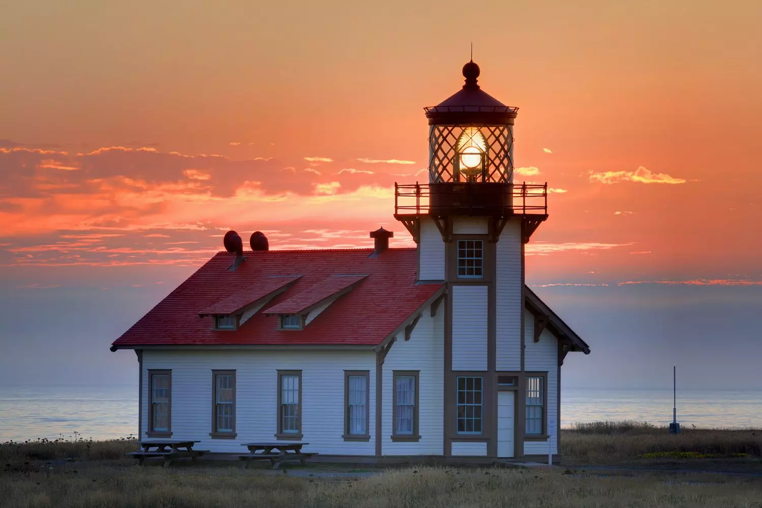 Silhouette of a lighthouse against a vibrant sunset, the sky painted in orange, pink and purple hues, the Pacific Ocean below, California