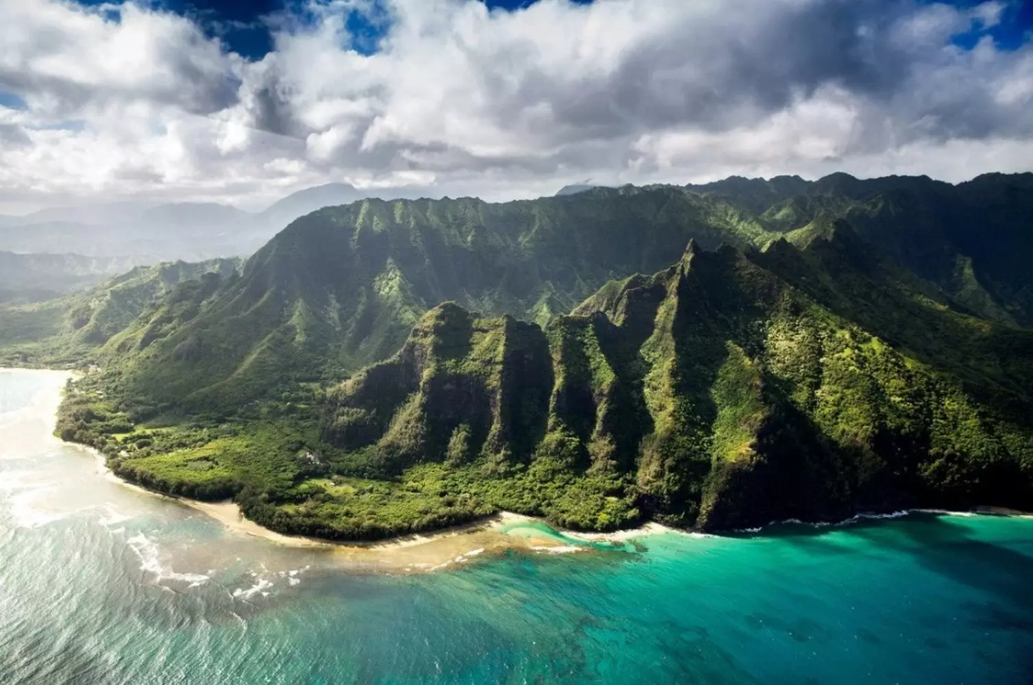 Aerial view of the Hawaiian Islands: Emerald Mountains, Turquoise Ocean and White Beaches Stunning aerial drone photo of the Hawaiian coastline showing lush green volcanic mountains meeting the bright turquoise coral reef and white sand beaches of the Pacific Ocean