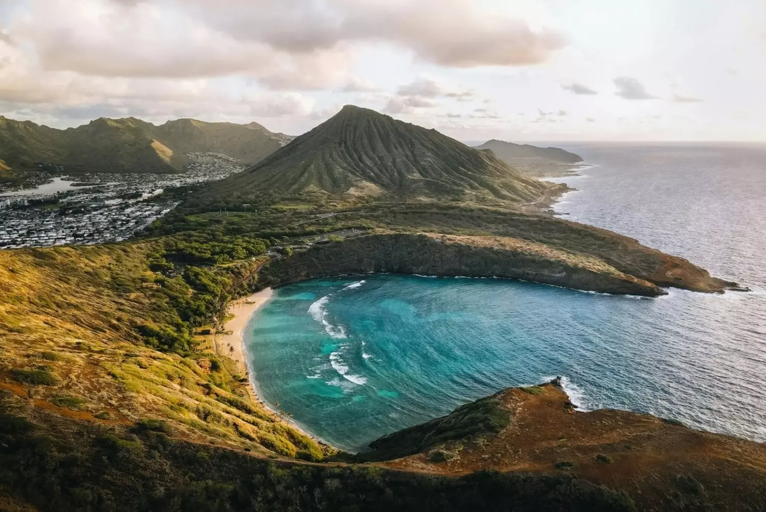 Aerial view of the Hawaiian Islands: Emerald Mountains, Turquoise Ocean and White Beaches Stunning aerial drone photo of the Hawaiian coastline showing lush green volcanic mountains meeting the bright turquoise coral reef and white sand beaches of the Pacific Ocean