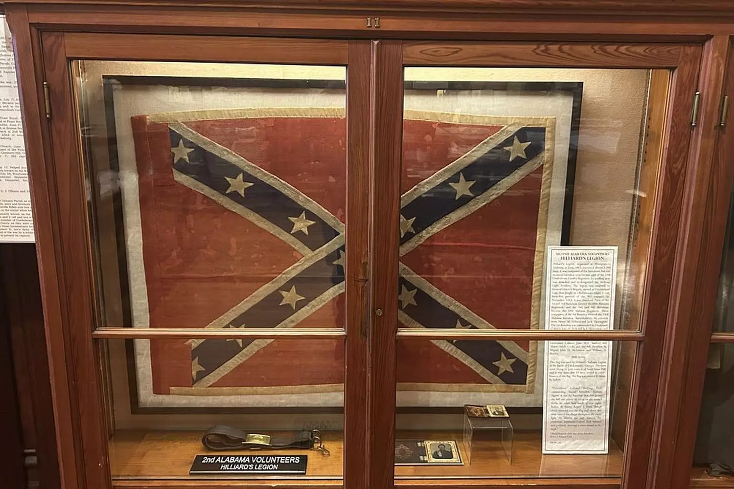 Стеклянная витрина с боевым флагом Конфедерации в музее Confederate Memorial Hall в Новом Орлеане: выцветшая ткань, нашитые звезды и музейная этикетка