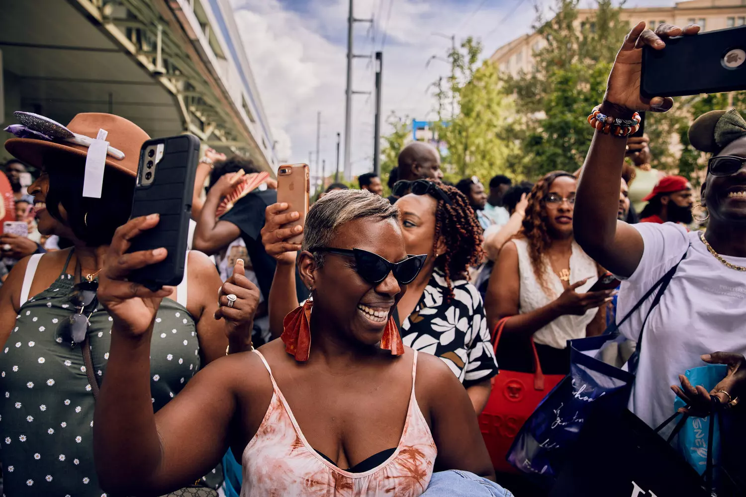 Толпа людей на улице во время Essence Festival, люди поднимают руки, танцуют и улыбаются, флаги и украшения, солнечная погода