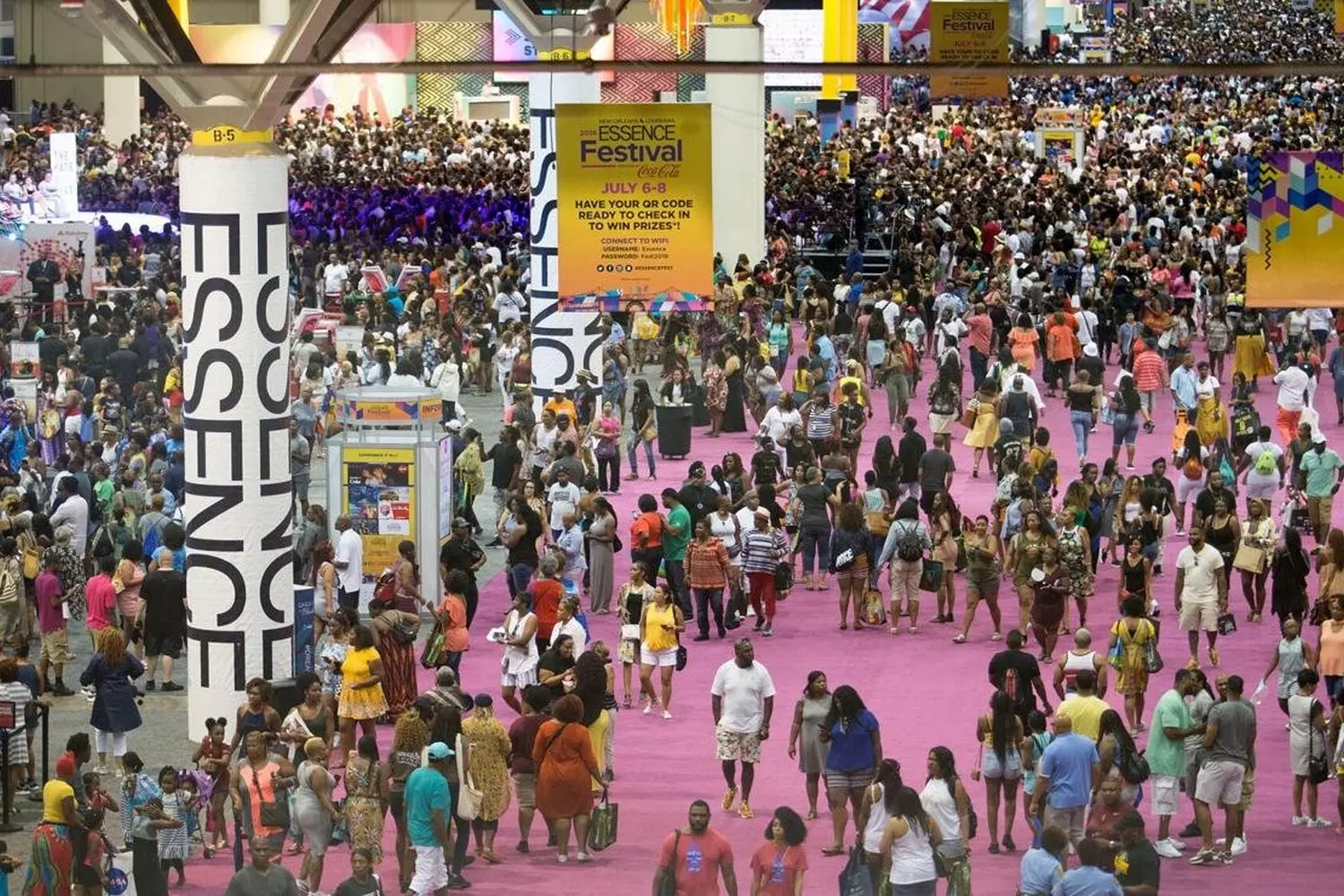 Огромная толпа людей на улице Нового Орлеана во время Essence Festival, люди танцуют и общаются, яркие наряды, городские здания на заднем плане