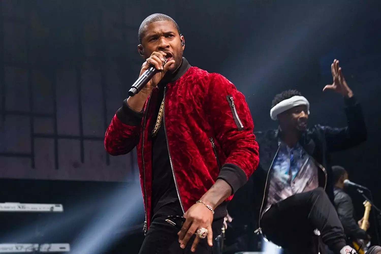 Ашер на сцене Essence Festival в Superdome, поет в микрофон, яркое сценическое освещение, толпа зрителей, церковный декор сцены