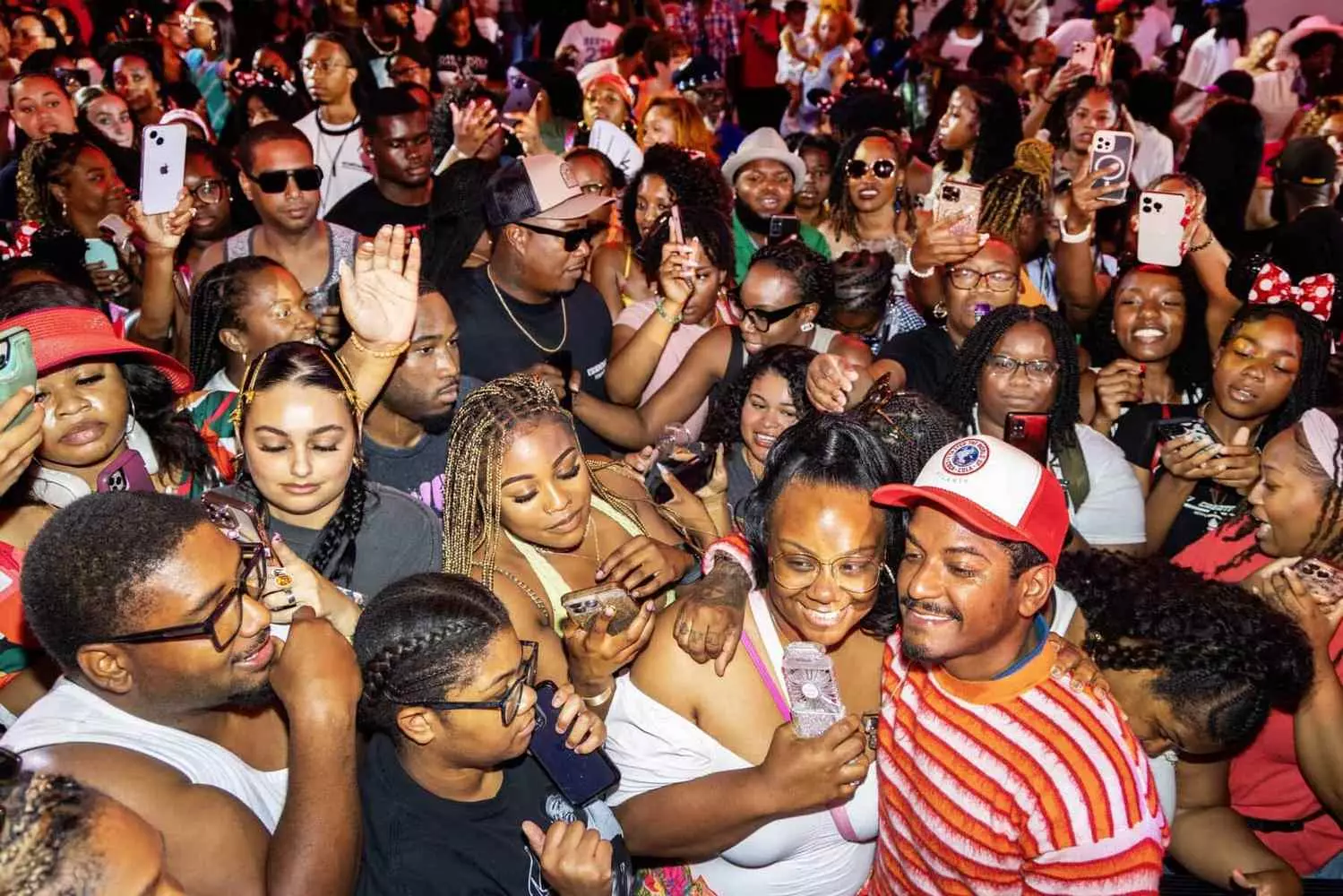 Толпа зрителей на Essence Festival в Mercedes-Benz Superdome, руки подняты в воздух, лазерные лучи сцены, тысячи фанатов в яркой одежде