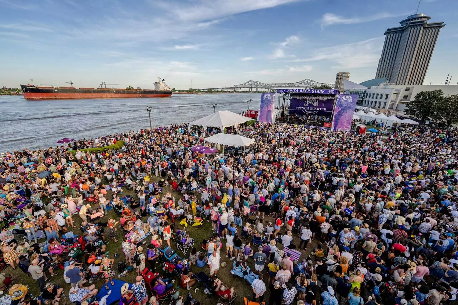 Панорама French Quarter Festival в Новом Орлеане — многотысячная толпа на набережной на фоне моста и барж на реке Миссисипи