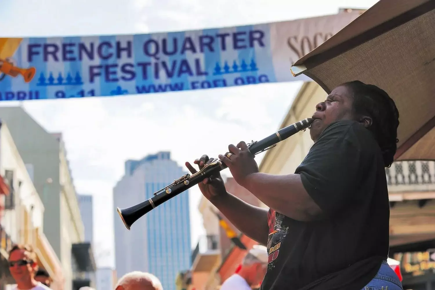 Уличный музыкант играет на флейте во время French Quarter Festival в Новом Орлеане на фоне исторической архитектуры Французского квартала