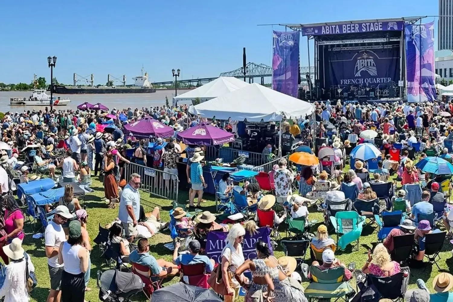 French Quarter Festival в парке Вольденберг, музыкальная сцена и толпа зрителей на фоне реки Миссисипи во время ежегодного апрельского фестиваля в Новом Орлеане