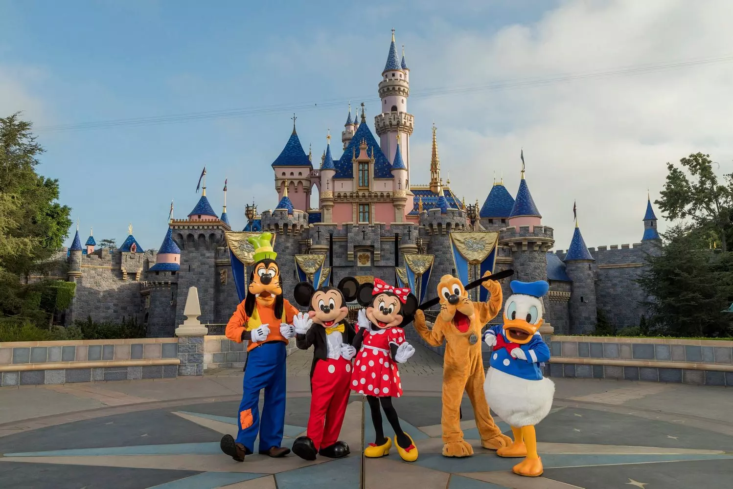 Magical Meet & Greet: Disney Character Costumes Pose in Front of the Iconic Disneyland Castle Colorful Disney character costumes (Mickey Mouse, Minnie Mouse, and other favorites) waving and smiling in front of the fairy-tale Disneyland castle, with crowds of visitors in the background